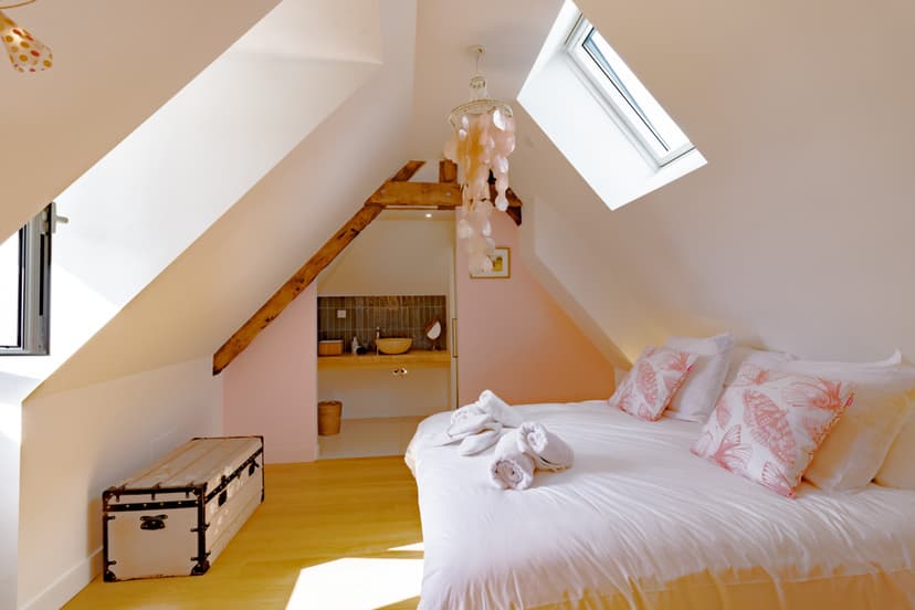 Chambre mansardée avec lit double, sol jaune, poutre apparente et salle de bain ouverte dans gîte de luxe