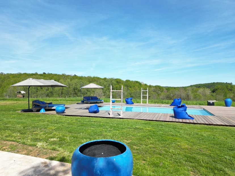 Villa de vacances avec piscine, transats bleus, parasols et vue sur la campagne verdoyante de Dordogne