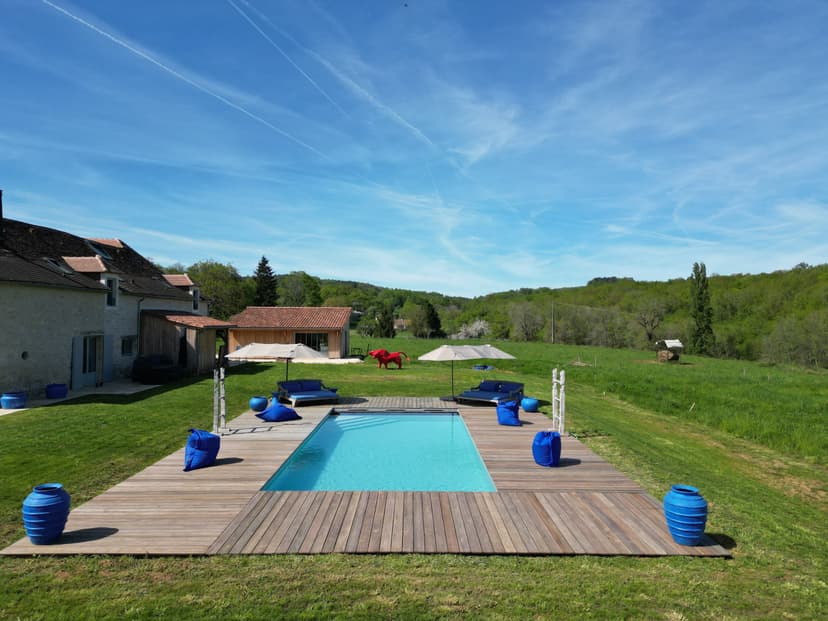 Piscina privada com deck em madeira, guarda-sóis e decoração azul em propriedade rural na Dordonha sob céu azul