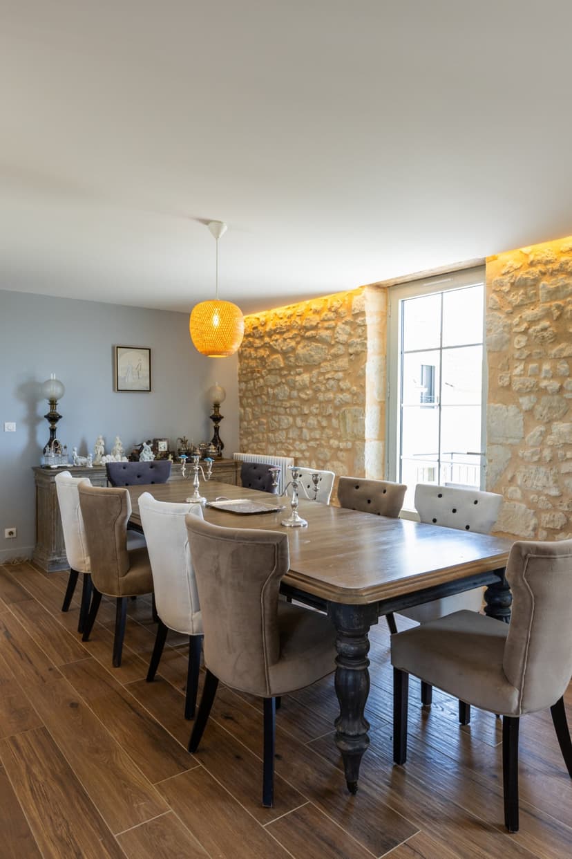 Élégante salle à manger avec table en bois, chaises beiges, mur en pierre apparente et lustre orange moderne