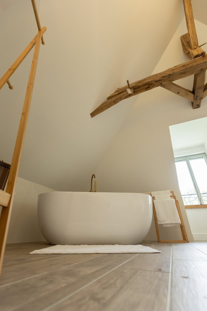 Modern wit bad onder dakbalken met houten balken en decoratieve ladder in vakantieaccommodatie