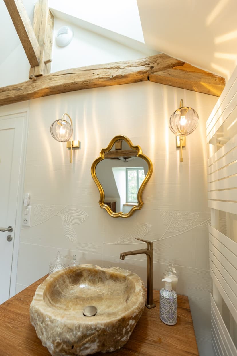 Elegante badkamer met stenen wasbak, zichtbare balken, gouden spiegel en designlampen in vakantiehuis