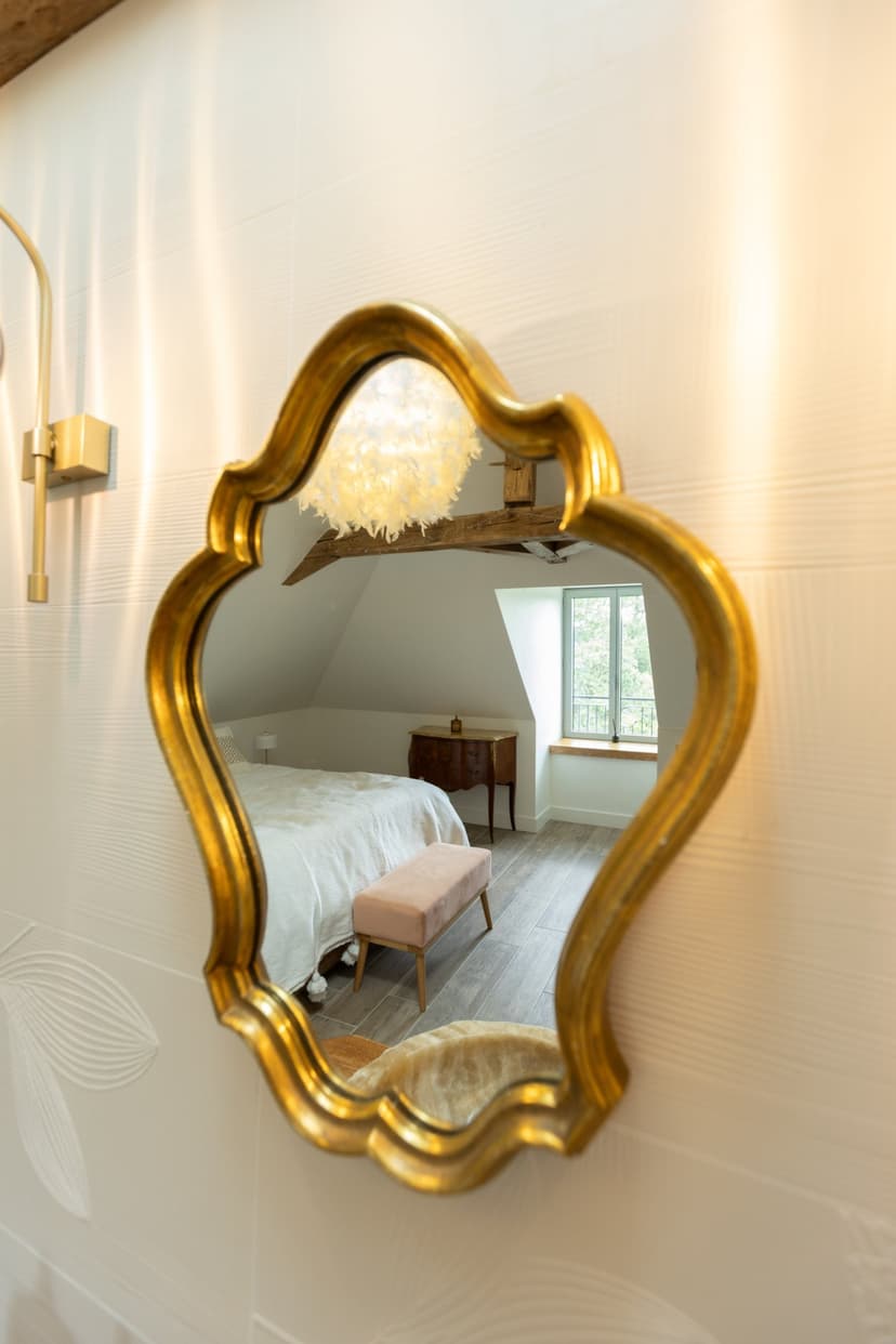 Quarto luxuoso com grande espelho barroco dourado refletindo uma cama branca e luminária moderna em parede texturizada branca