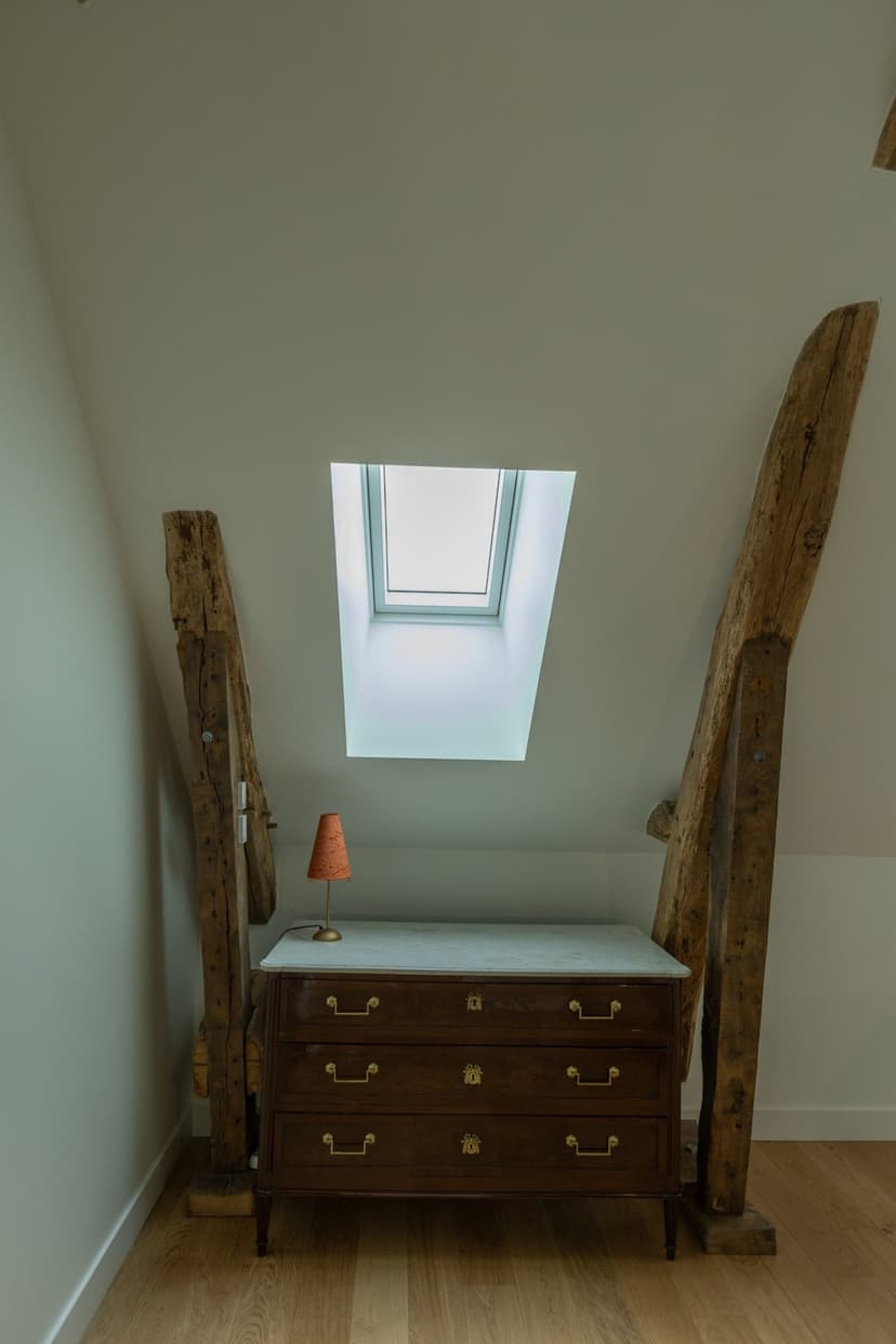 Quarto sob telhado com vigas em madeira, cômoda antiga e claraboia em moradia de luxo na Dordonha