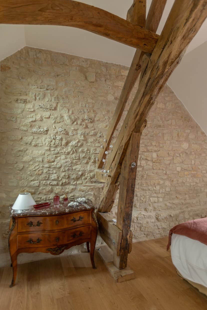 Rustikales Interieur mit freiliegenden Holzbalken, Steinwand und antiker Kommode in einer Luxusunterkunft