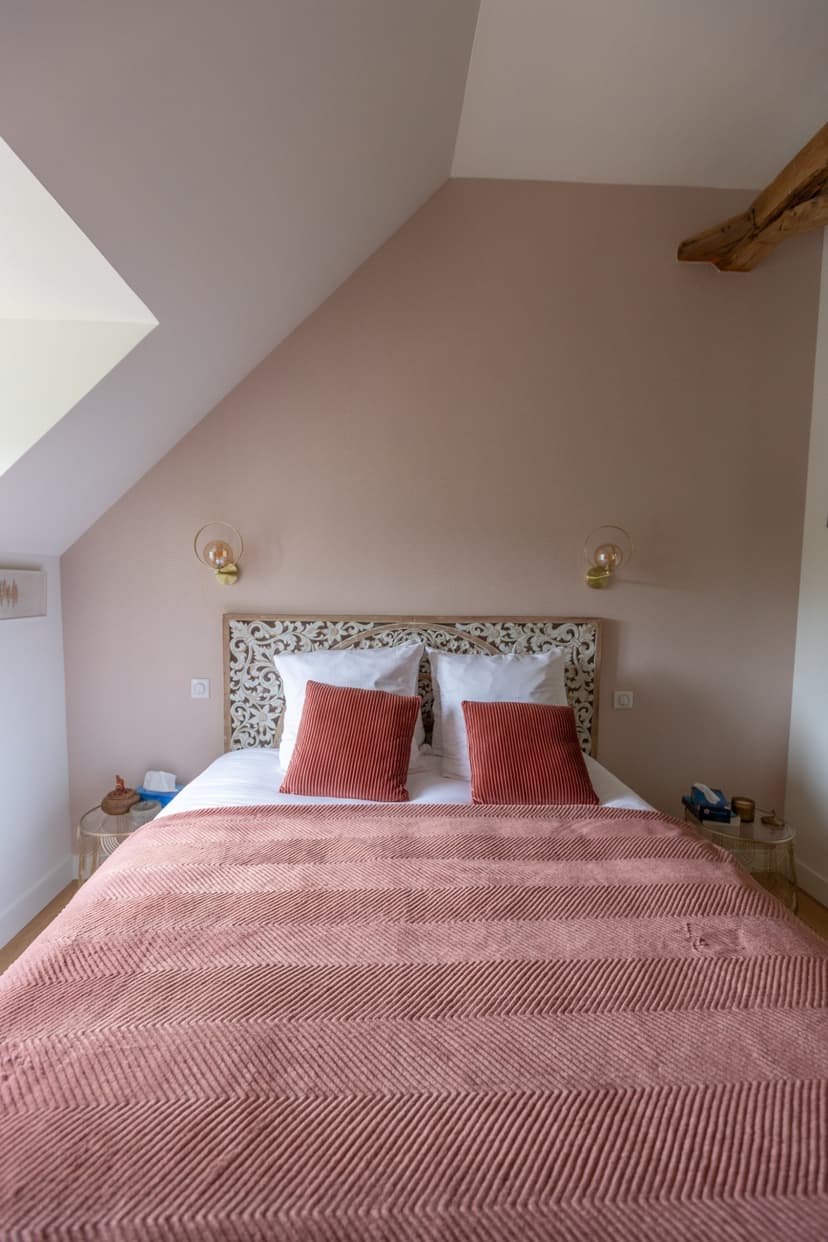 Cosy bedroom with double bed, coral linen, sculpted headboard and pink walls under mansard roof