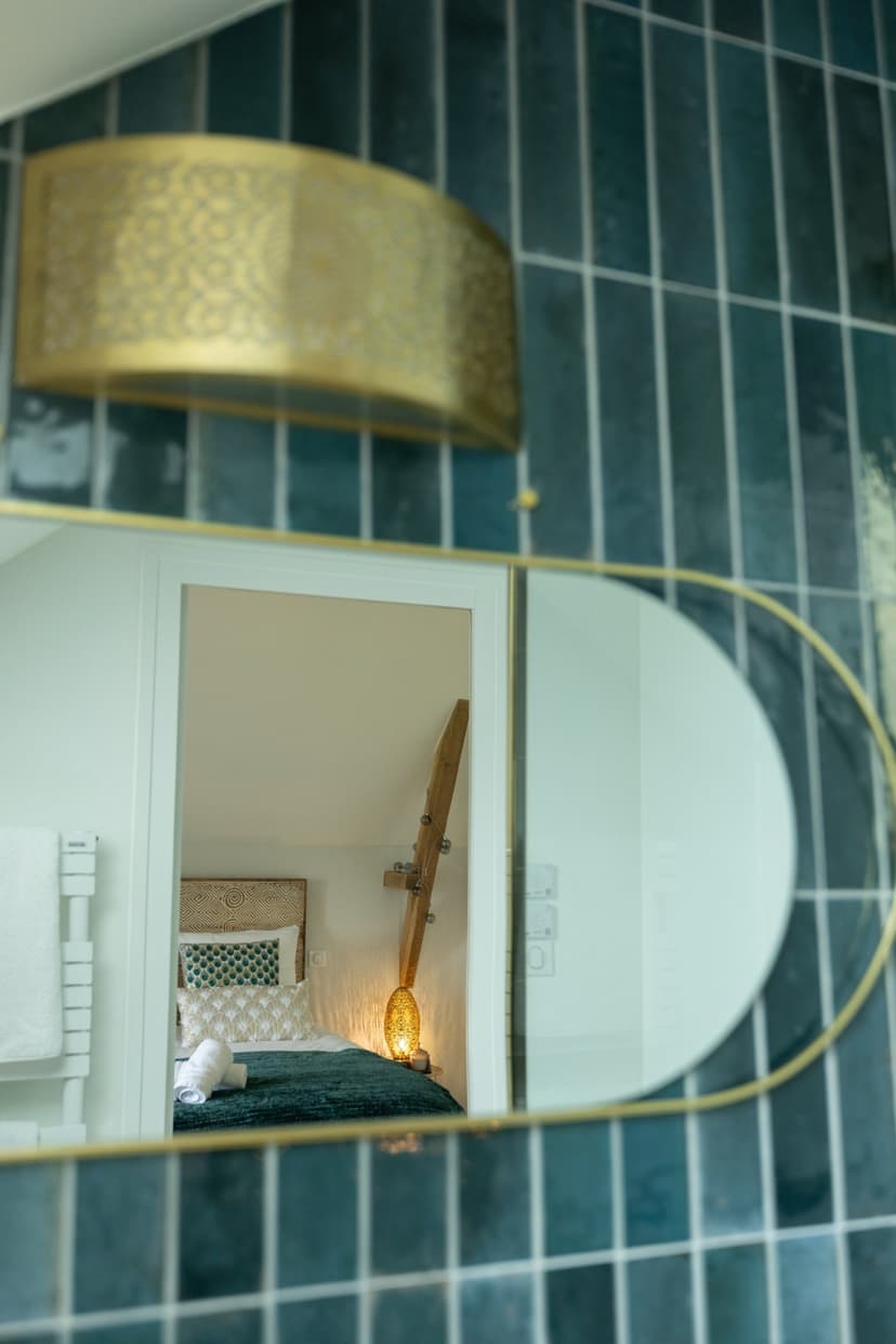 Ronde gouden spiegel in turquoise betegelde badkamer met zicht op elegante slaapkamer in groene tinten