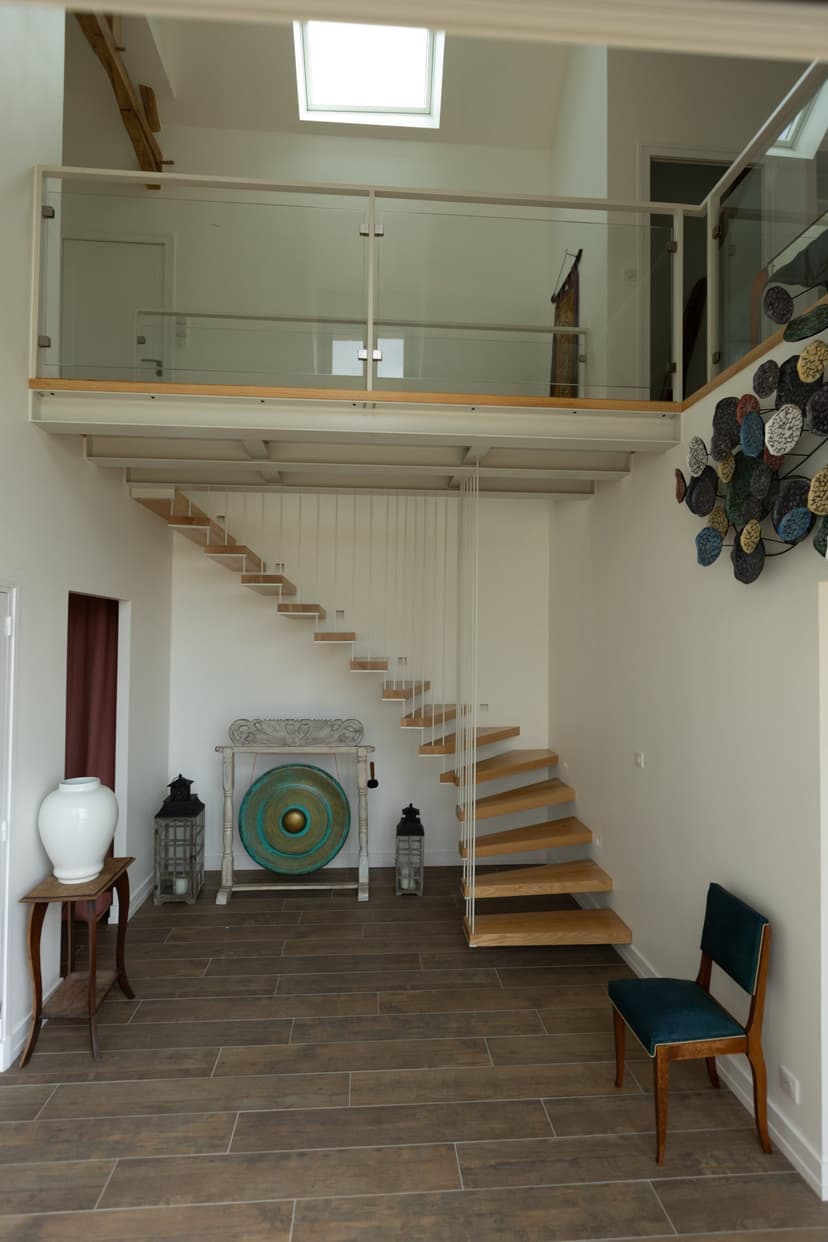 Intérieur spacieux d'une villa avec escalier suspendu, mezzanine vitrée, décoration contemporaine et carrelage sombre