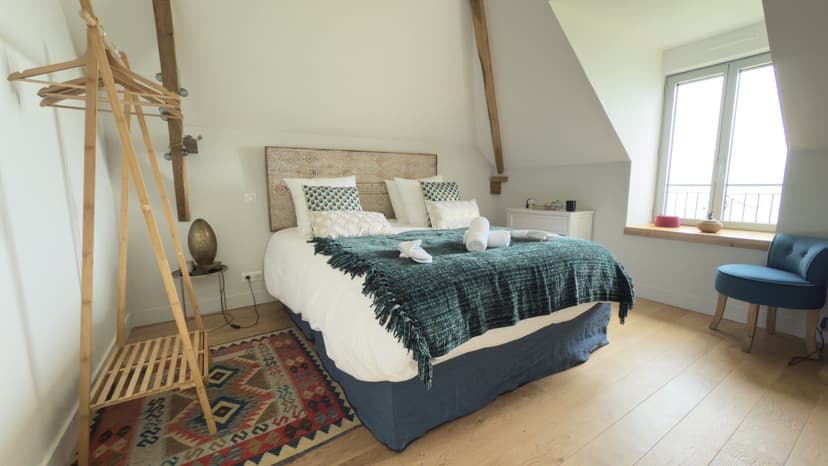 Elegante habitación con cama doble, vigas de madera, alfombra kilim colorida y sillón azul en casa de vacaciones