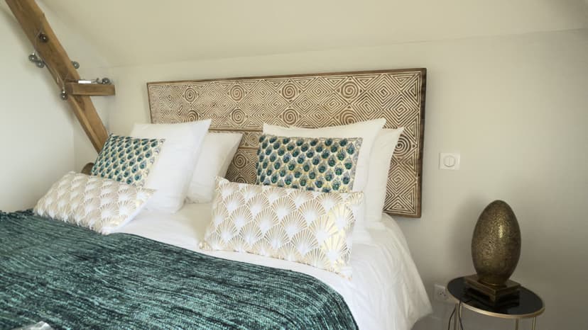 Elegantes Zimmer mit Kopfteil in geometrischen Mustern, bunten Kissen, sichtbarem Holzbalken und raffinierter Dekoration