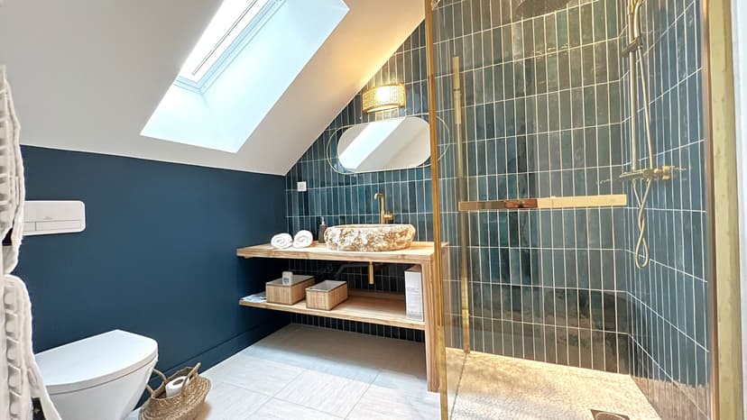 Moderne badkamer met blauwe tegels, stenen wastafel, gouden douche en lichtkoepel in zolderverdieping