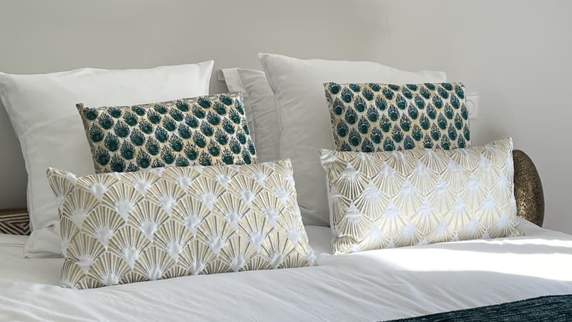 Cama de casal com almofadas brancas e almofadas decorativas com motivos geométricos dourados e verdes em propriedade de luxo