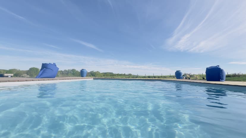 Grande piscina cristalina com vista sobre o campo da Dordonha, guarda-sóis azuis e reservatórios de água ao fundo