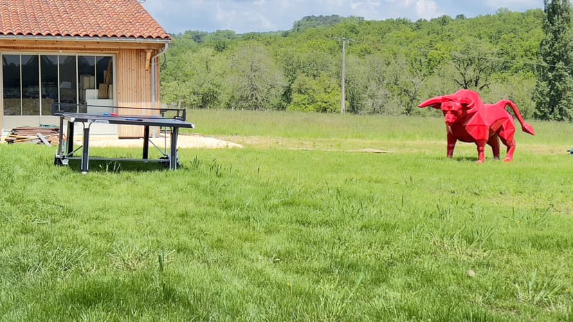 Modernes Holzferienhaus mit Ziegeldach, Tischtennisplatte und roter Elefantenskulptur in einem Garten