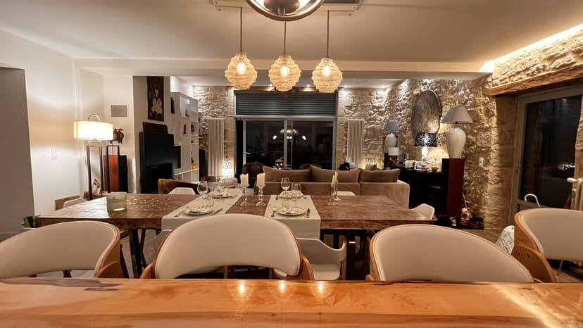 Intérieur luxueux avec salle à manger, mur en pierre apparente, suspensions design et salon cosy en arrière-plan