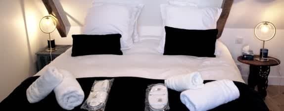 Elegante slaapkamer met tweepersoonsbed, wit linnen, zwarte kussens, houten balken en designlampen in accommodatie Dordogne
