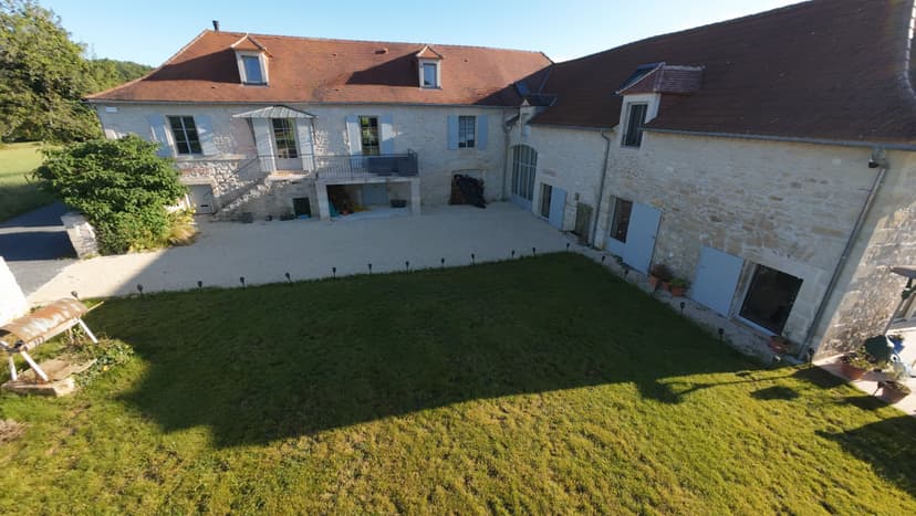 Vue aérienne d'une maison traditionnelle en pierre avec toit de tuiles, cour pavée et pelouse en Dordogne