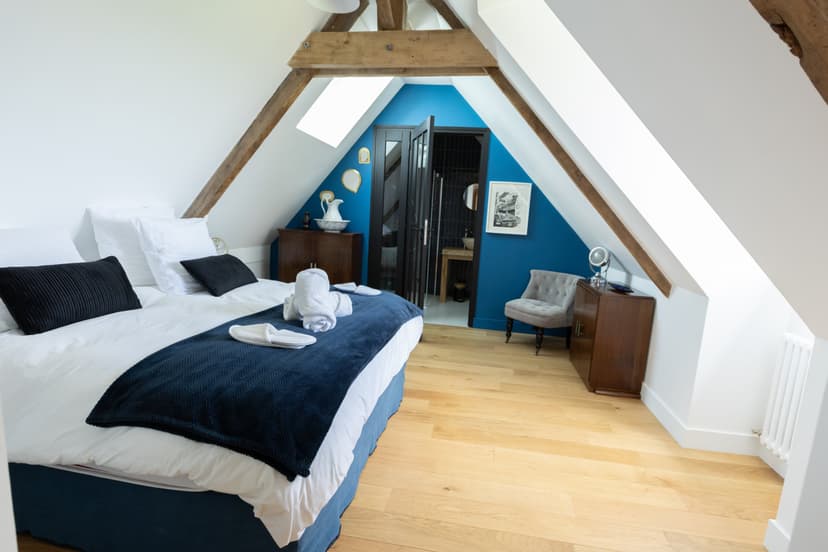 Elegantes Zimmer unter dem Dach mit Holzbalken, blauer Wand, Doppelbett und Sitzecke in Ferienunterkunft