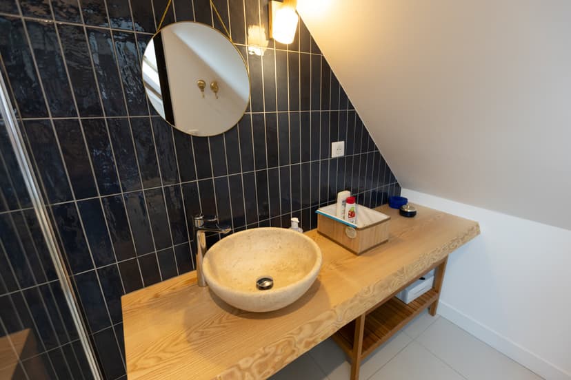 Baño lujoso con lavabo redondo de piedra, encimera de madera, azulejos negros y espejo redondo suspendido