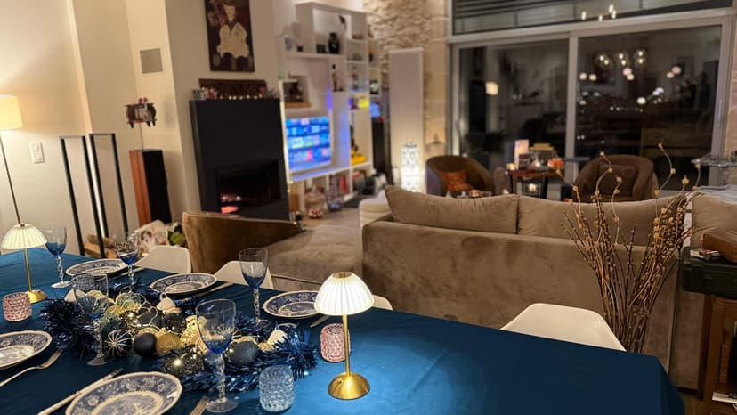 Salón moderno con sofá gris, mesa vestida en azul y blanco, vista sobre terraza iluminada por la noche
