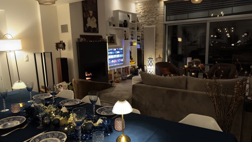Modern living room with grey sofa, fireplace, set table and night view in luxury villa in Dordogne